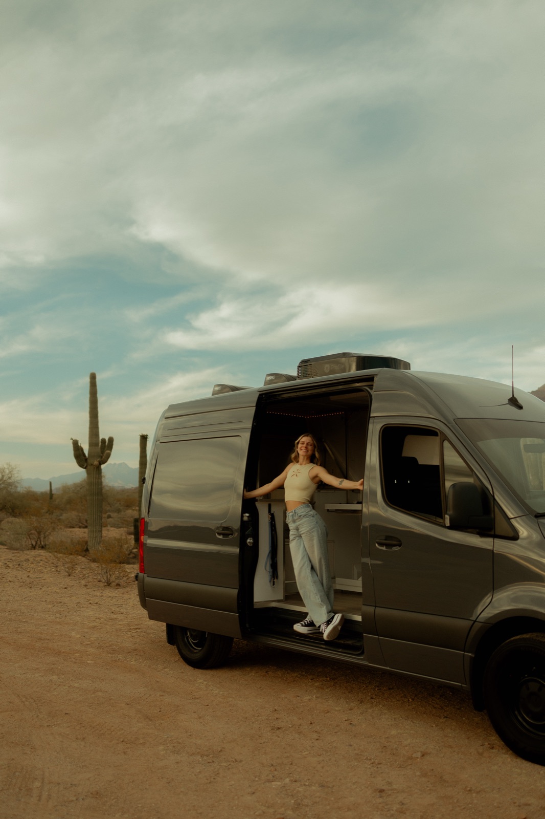 Maddison Hess smiling in the open doorway of her grooming van, parked in the desert with a saguaro behind her